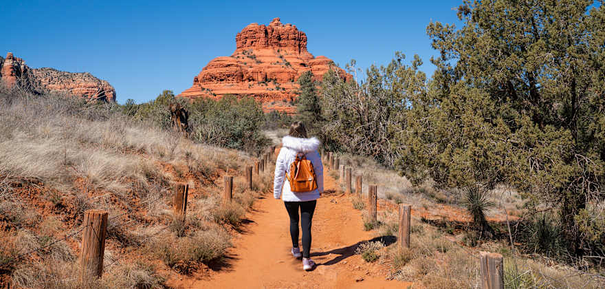 A person in a white coat walks on the Bell Rock Pathway in Sedona, Arizona.