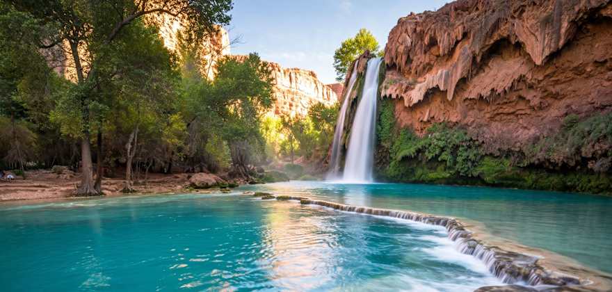 Turquoise water beneath Havasu Falls in Arizona surrounded by red rock and greenery.