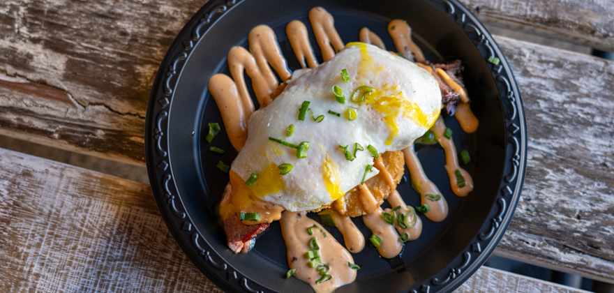 a black plate with hash browns topped with eggs and a creamy sauce on a wooden table