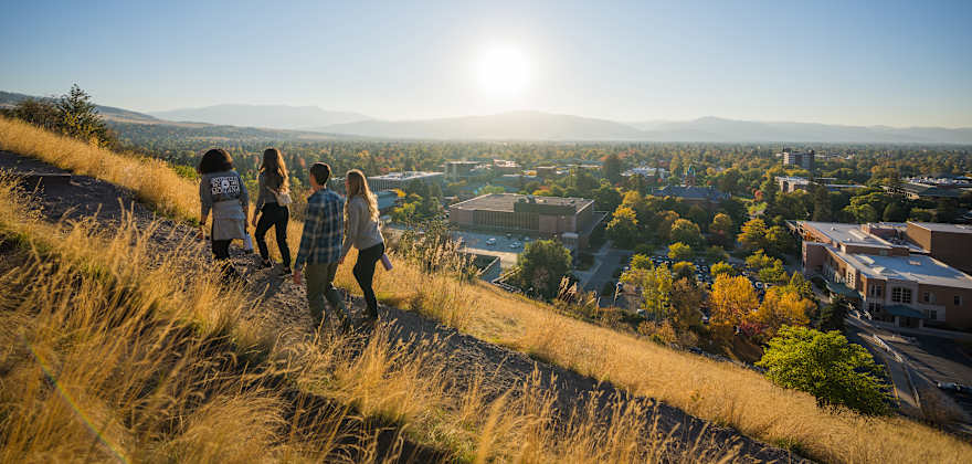 four people hike up a mountain with dry grass and a view of Missoula, Montana