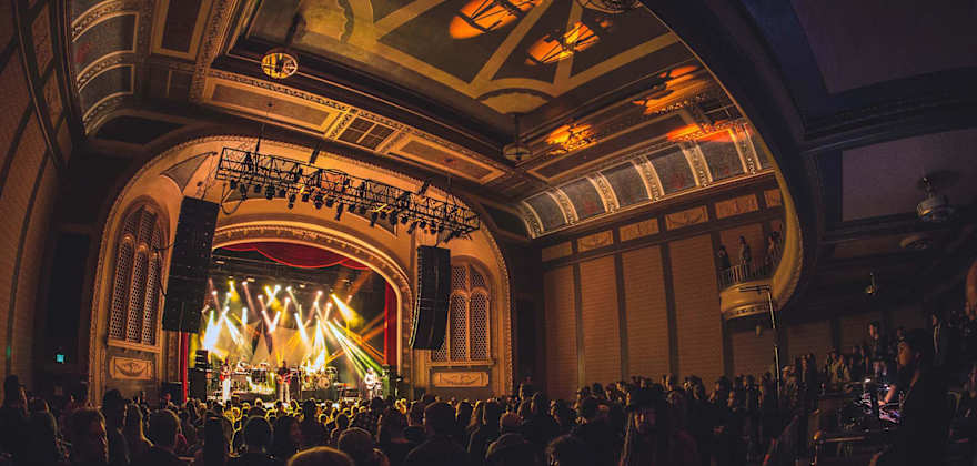 a packed concert hall with an ornate ceiling