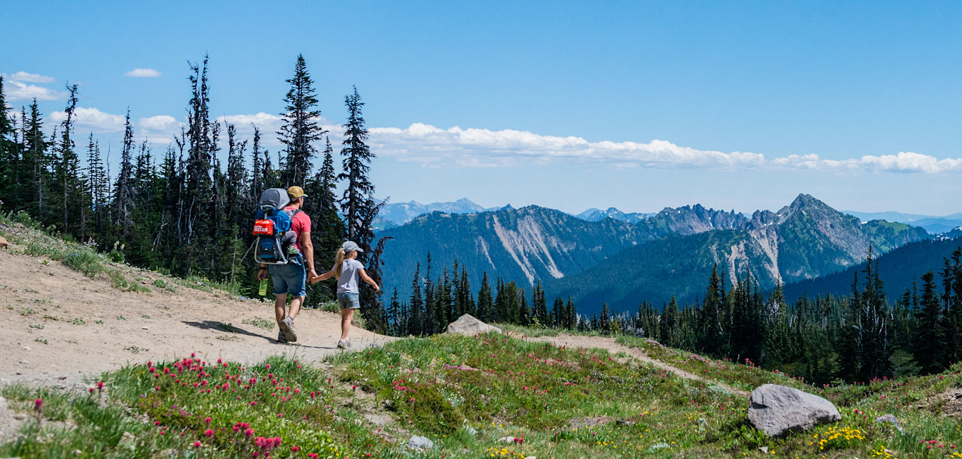 a parent and young child hike with backpacks in view of snowy mountains