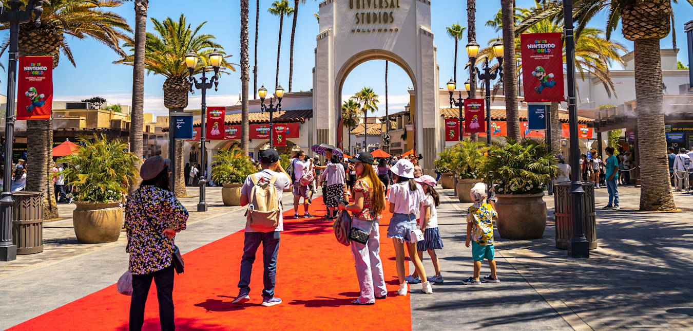 people walk towards Universal Studios Hollywood on a red carpet surrounded by palm trees