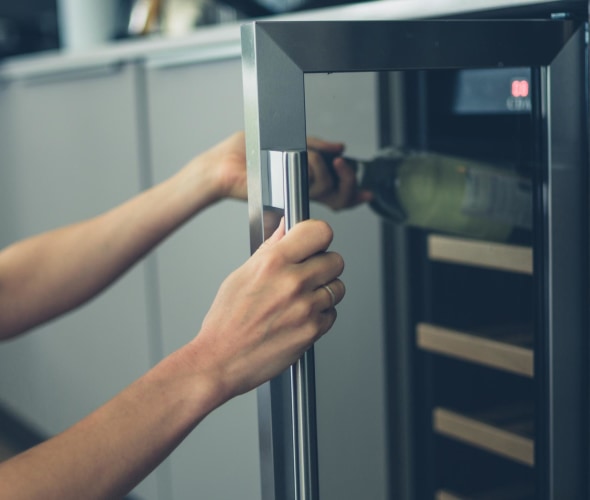 A woman's arm reaches into a wine fridge to remove a bottle of white wine, picture