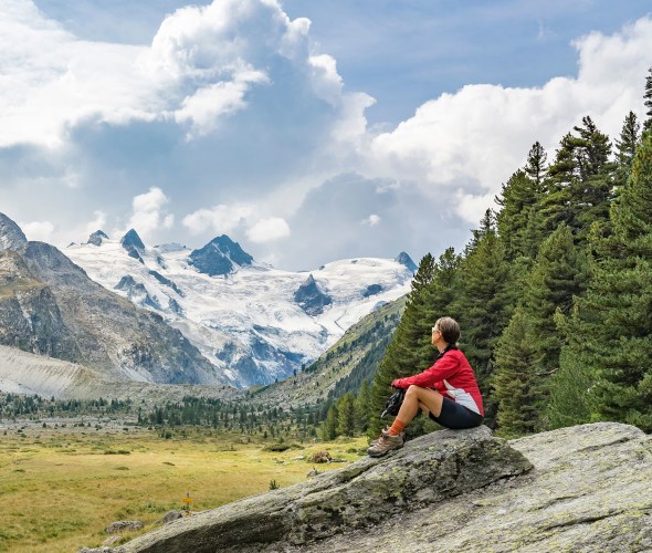 picture of a hiker sitting and looking out at a scenic valley with a mountain in the background