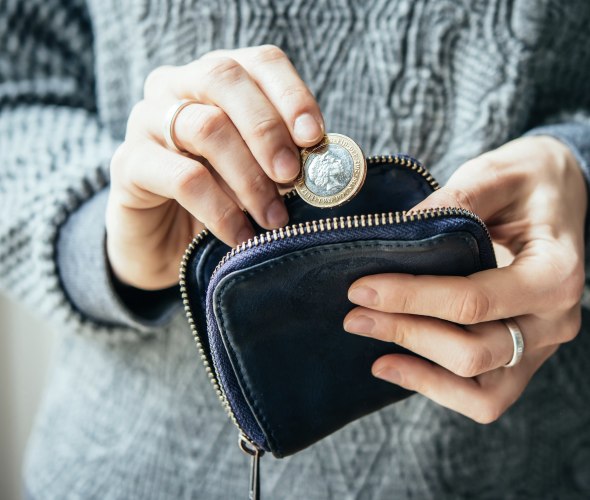 A woman in a thick gray sweater puts euros into a purse.