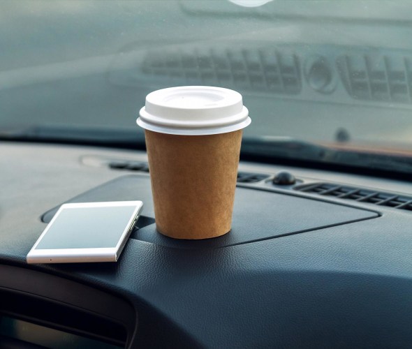 A cell phone and a cup of coffee sit on top of a car dashboard.