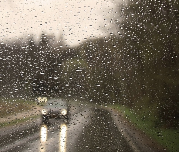 car driving on a wet road seen through a rainy windshield