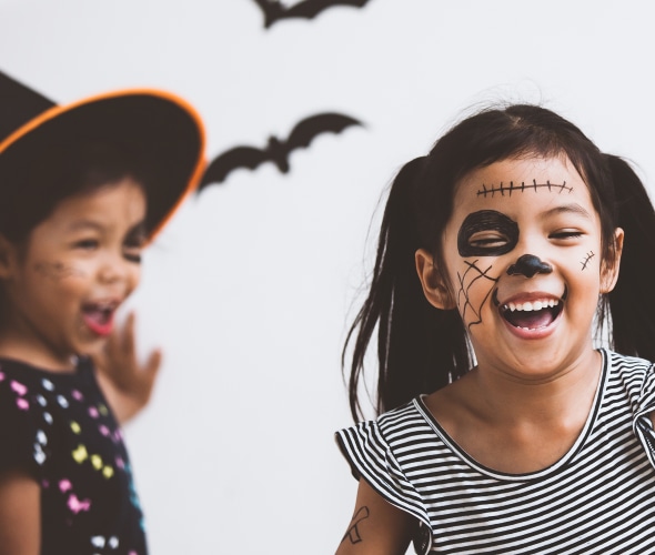 Two girls with face paint put up Halloween decorations bats