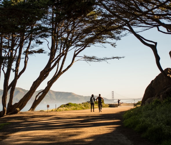 picture of a couple walking a path in the presidio with the golden gate bridge in the background