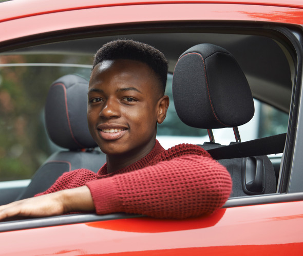 Teen in the drivers seat of a red car.