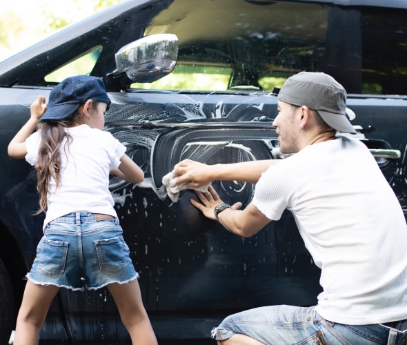father and daughter in jeans, t-shirts-and baseball hats wash the exterior of the family car