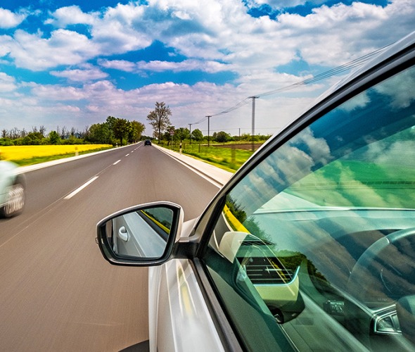 A speeding car passes another car on the left with partially cloudy blue skies