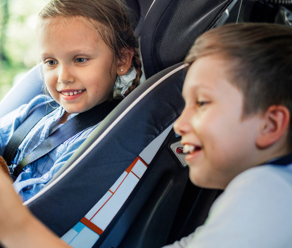brother and sister look at a tablet in the backseat of a car