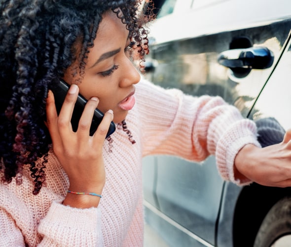 A female college student inspects damage to her call while on the phone with her insurance agent