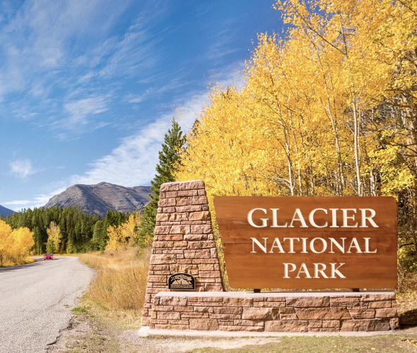 dramatic fall color and a flagstone sign beside road greet visitors at Glacier National Park's west entrance in Montana