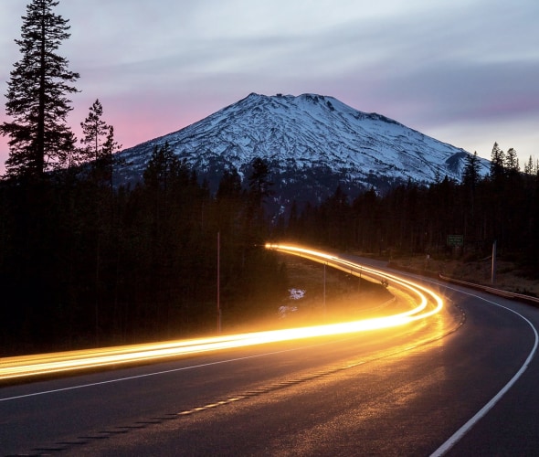 oncoming traffic headlight trails bend along a mountain highway at dusk