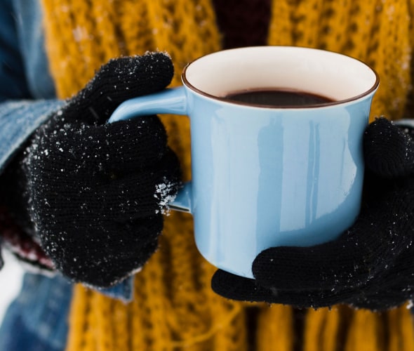 A person holds a blue coffee mug on a snowy morning.