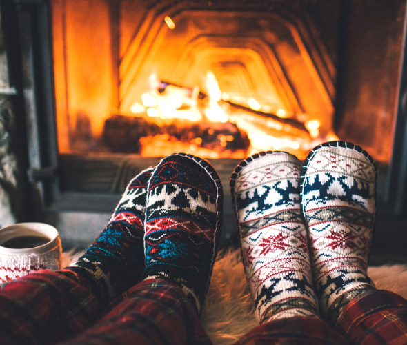 A couple warm their feet in front of a fire.