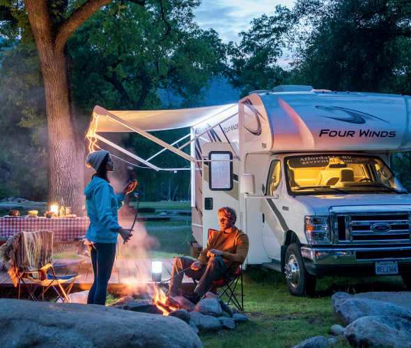 A couple relax around a campfire outside their RV