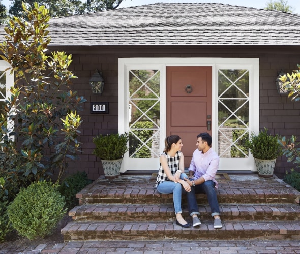 young couple sitting on brick steps outside their new home