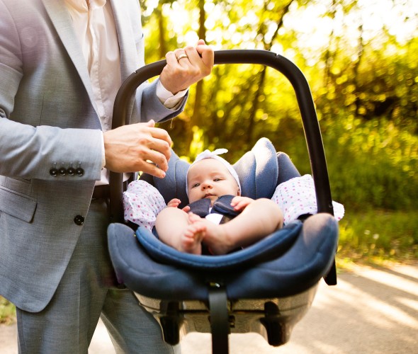 A father carries an infant in a car seat.