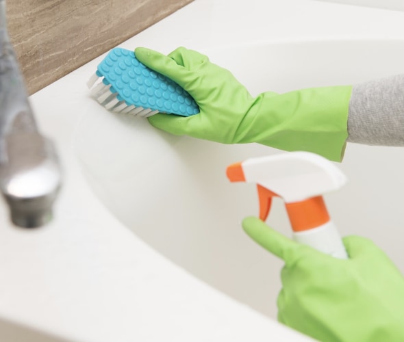 a gloved hand scrubbing a bathtub with a sponge and spray bottle