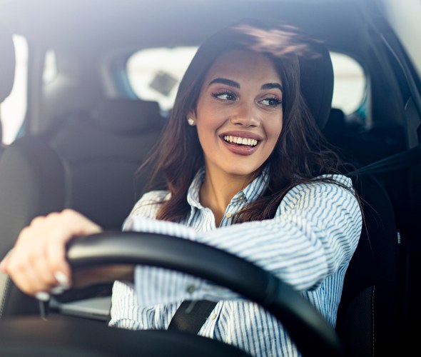 A woman smiles while driving a car.