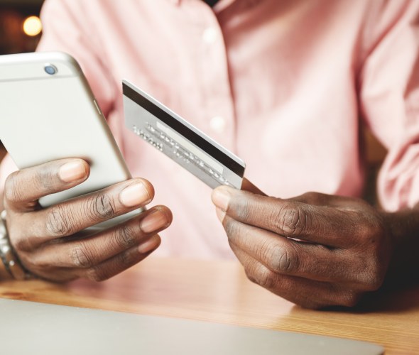 a black man uses a credit card to purchase something on his phone with coffee cup in foreground