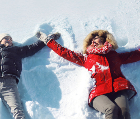 A mother and son make snow angles in winter coats.