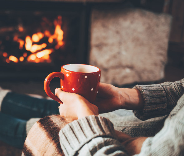 A peson sits in front of the fireplace with a mug of hot chocolate.
