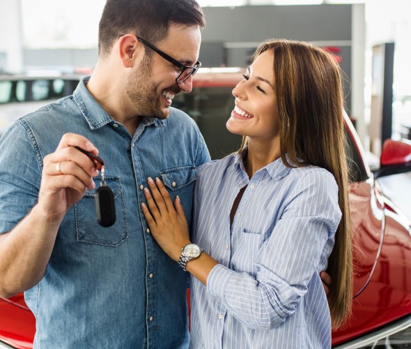 A couple hold the keys to their new red car in the dealership.