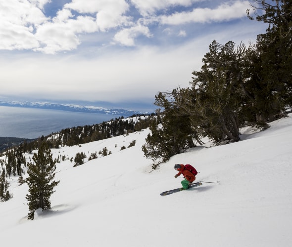 A skier rides down the mountain with views of Lake Tahoe in the background, image