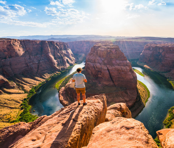 A tourist stands overlooking Horseshoe Bend on sunny day in Page, Arizona.
