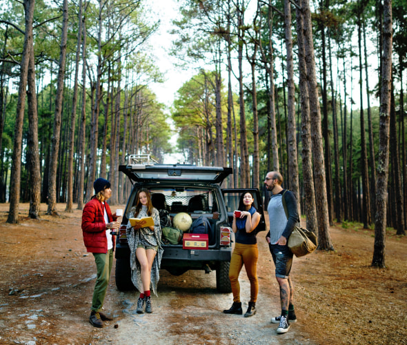 Friends stand around an open car tailgate with camping gear in the back, image