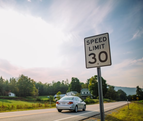 A car drives on a rural road under a 30 mph speed limit sign.