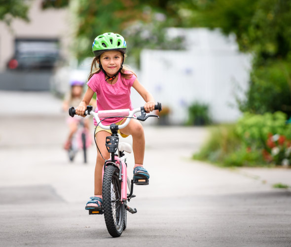 A young girl in pink rides her bike to school.