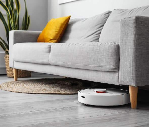 A smart robot vacuum cleans under a gray sofa.