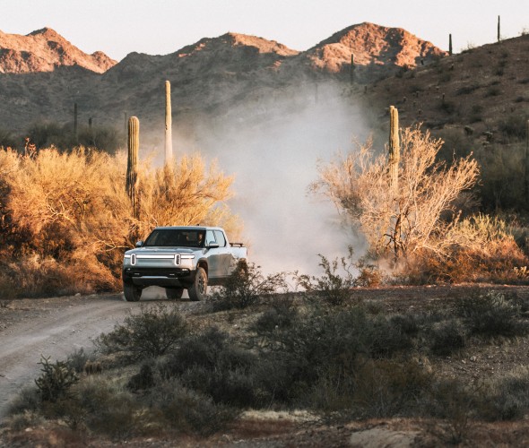 A Rivian truck drives off-road in the desert.