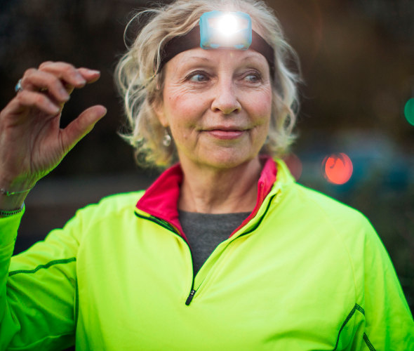A runner in a neon green shirt turns on her headlight.
