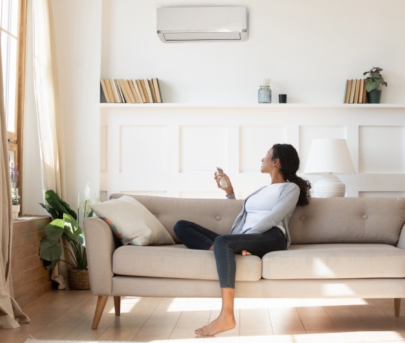 A woman turns on her mini split heat pump while sitting on the couch in the living room.