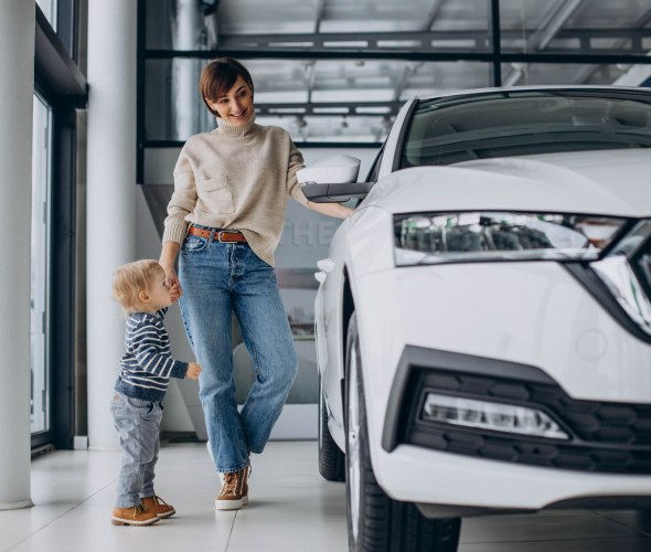 A mom and her child look at a white car in a dealership showroom.