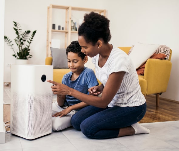 A mother and son turn on their air purifier in their living room.