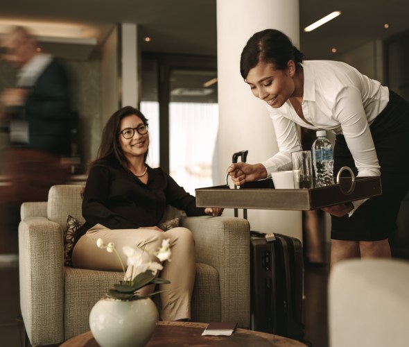 An airport lounge employee sets down a tray of drinks in front of a traveler.