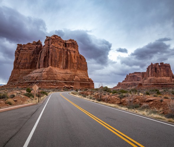 The Organ sandstone rock tower seen along Arches Scenic Drive with dramatic storm clouds looming overhead in Arches National Park, Moab, Utah.