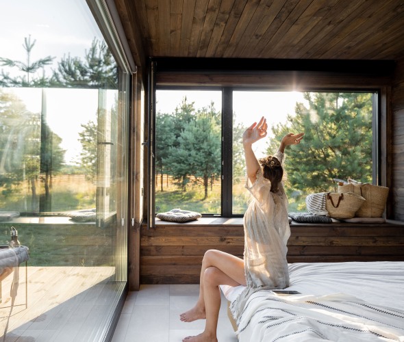 A woman stretches on her bed as morning light streams through the windows.
