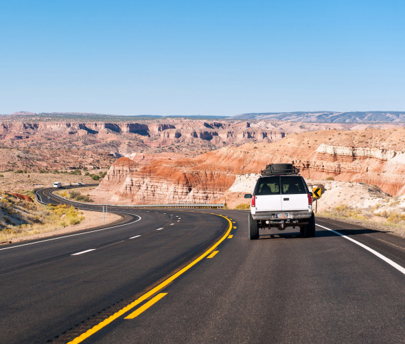 A white SUV drives through the Arizona desert on a sunny day.