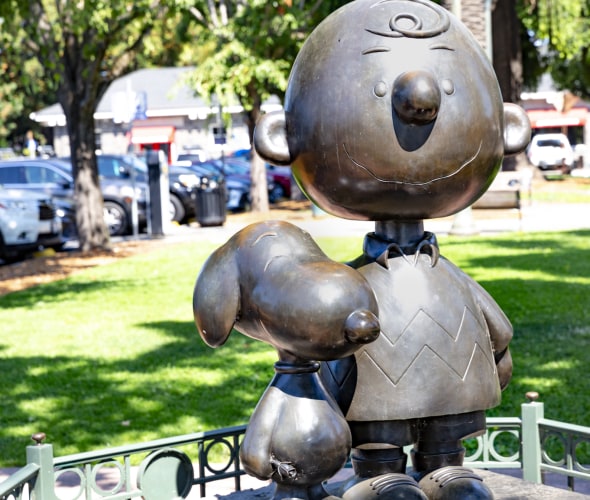 A lifesized bronze statue of the Peanuts' Charlie Brown and Snoopy in a park.