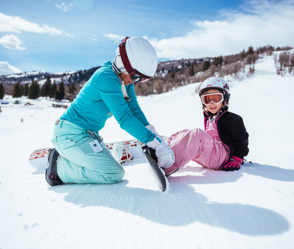 A woman helps a little girl put her boot back into her snowboard on the slope at Nordic Valley Ski Resort in Ogden, Utah.