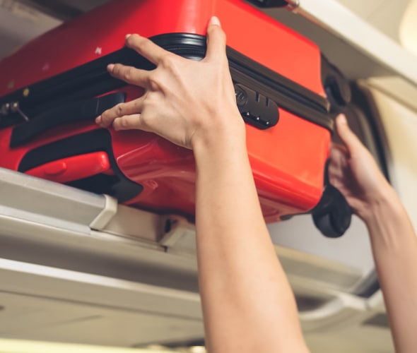A traveler puts their hard suitcase into the overhead bin of an airplane.